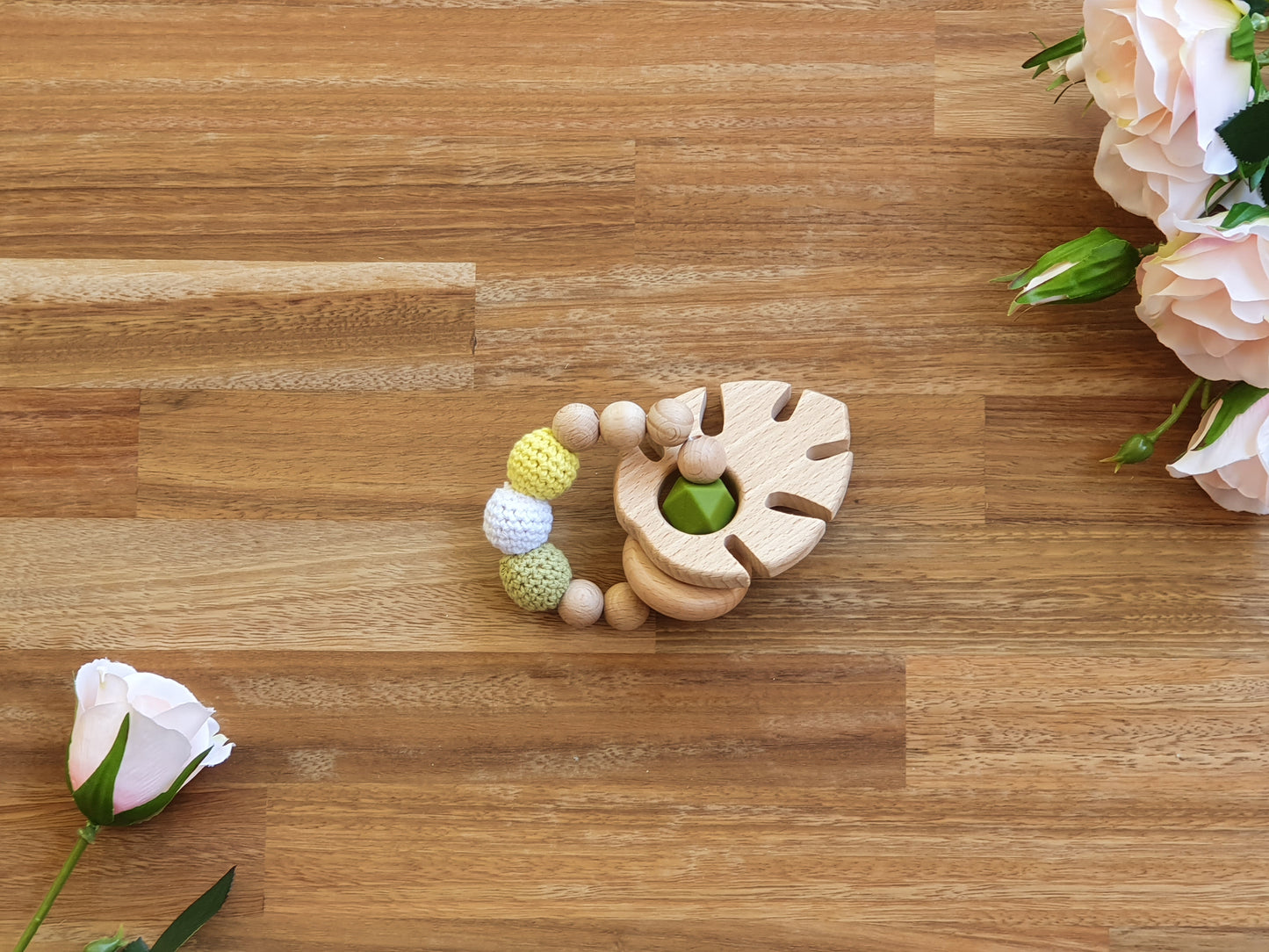 A wooden baby teether toy with textured beads in pastel yellow, white, and light green with a large wooden leaf.
