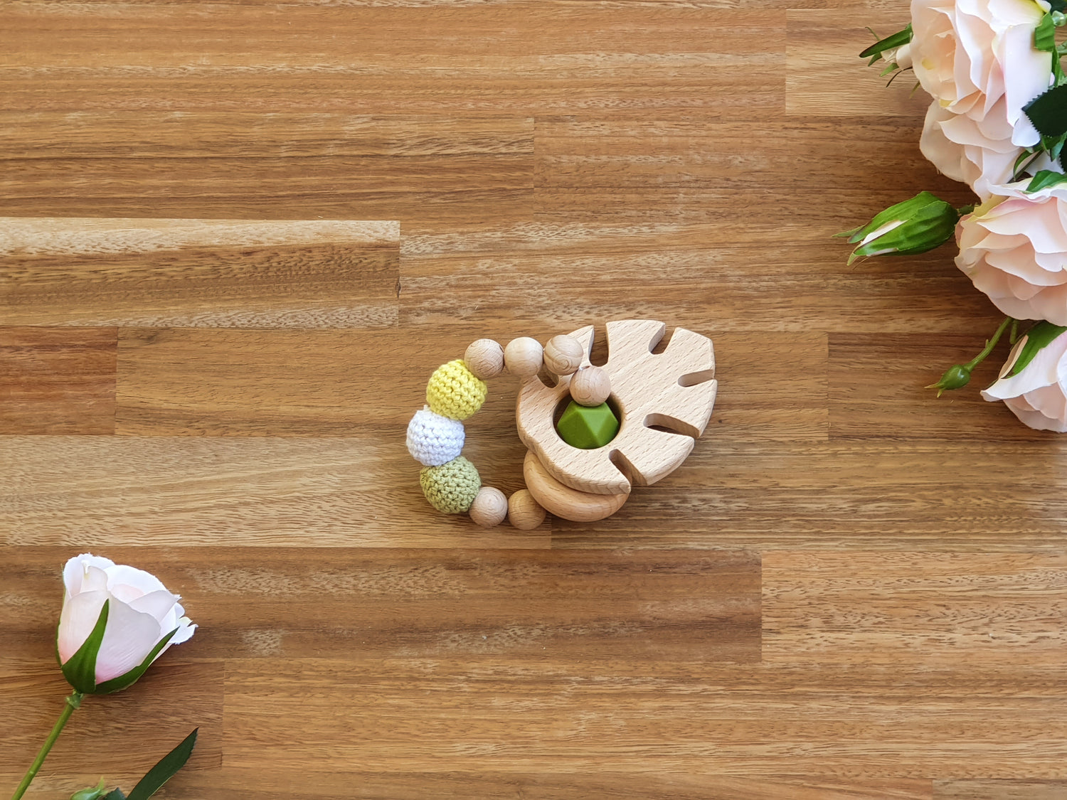 A wooden baby teether toy with textured beads in pastel yellow, white, and light green with a large wooden leaf.