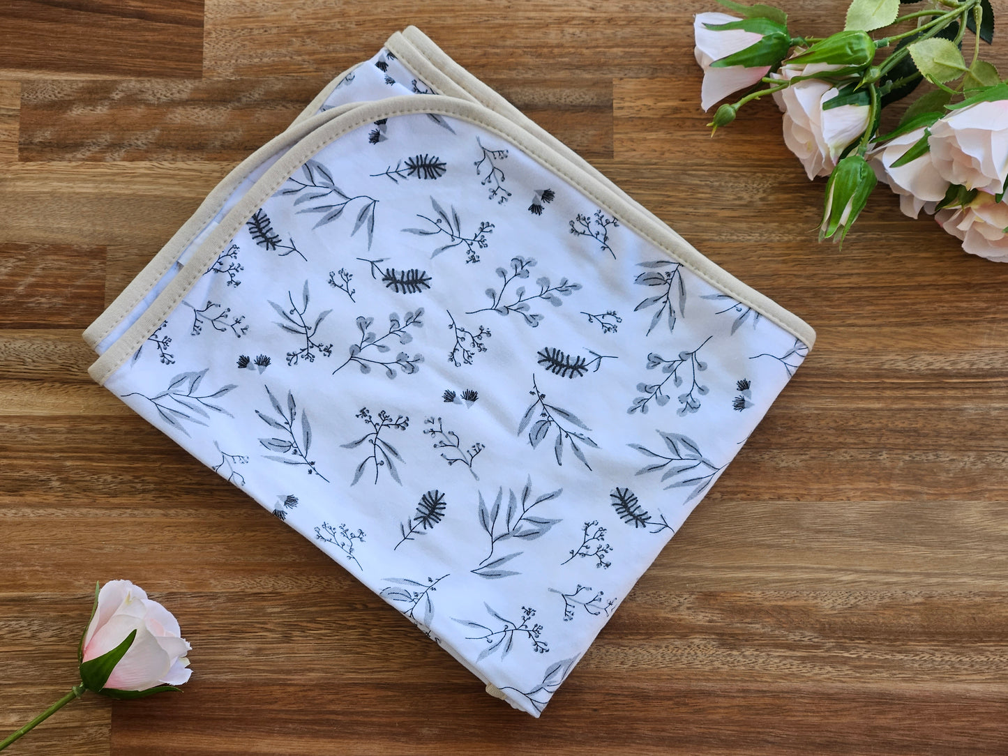 A folded white cotton baby blanket with a delicate grey botanical and leaf pattern.