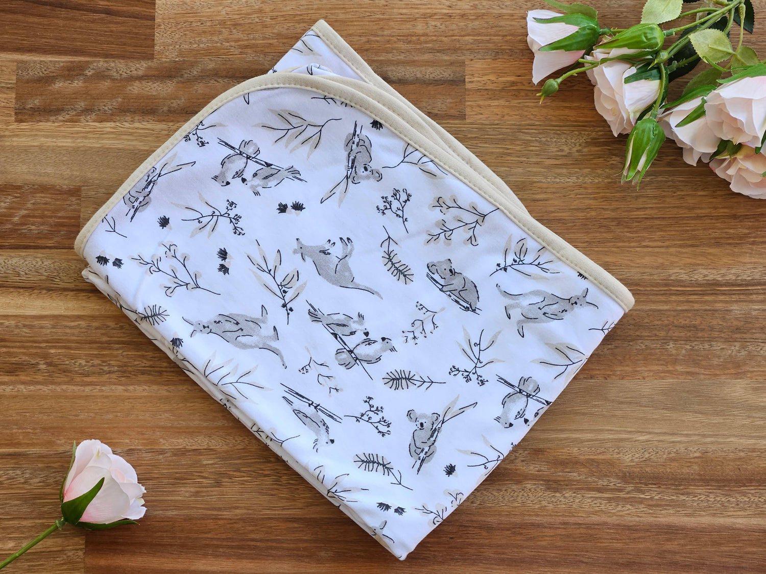 A folded white cotton baby blanket with a black and grey animal print, featuring a beige border.