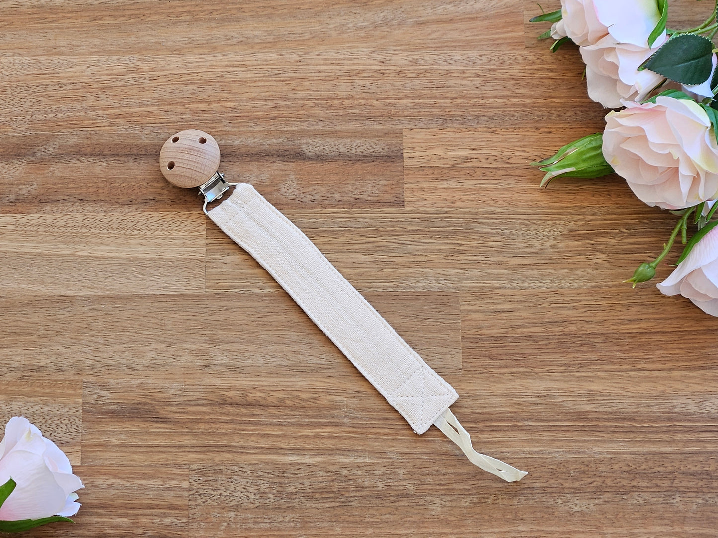 A beige colour muslin fabric pacifier clip with a natural wood ball clip.