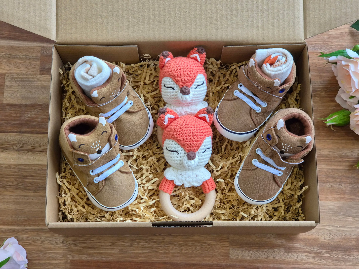 A baby gift box containing four brown Fox themed booties with white laces and 2 fox rattle toys.