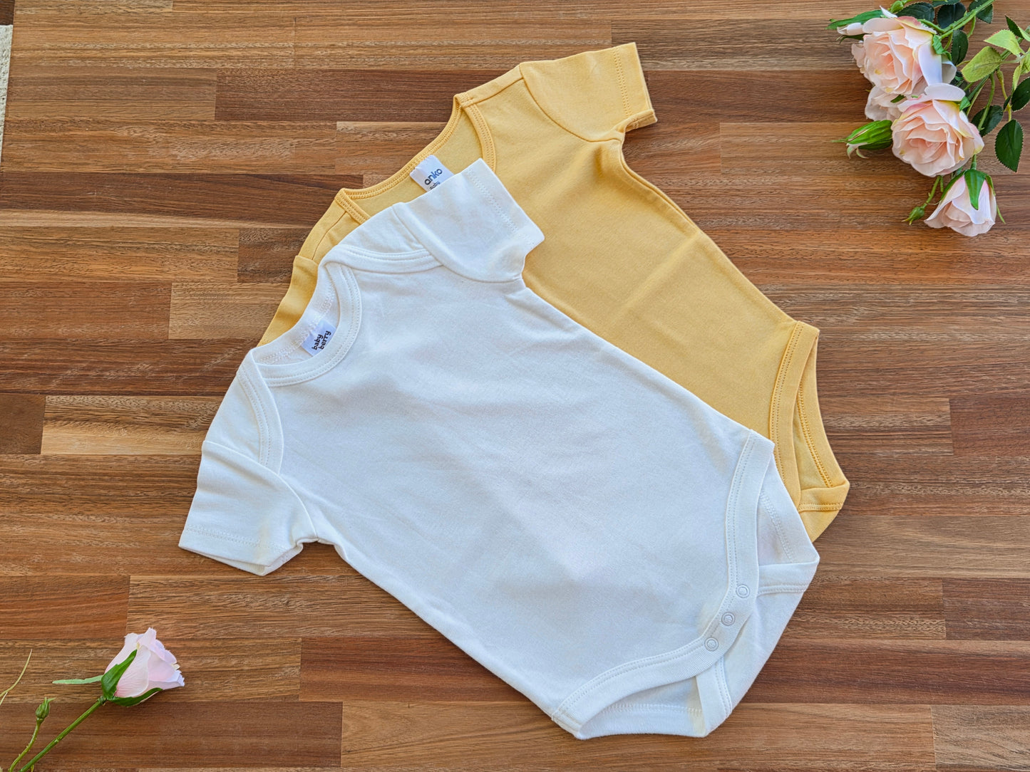 Two short-sleeve baby rompers, one white and one yellow.