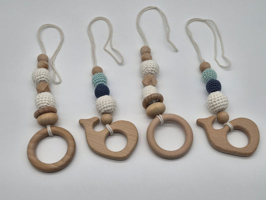 Four wooden baby gym hanging toys with knotted beaded straps, arranged on a wooden tabletop with pink flowers in the corners.