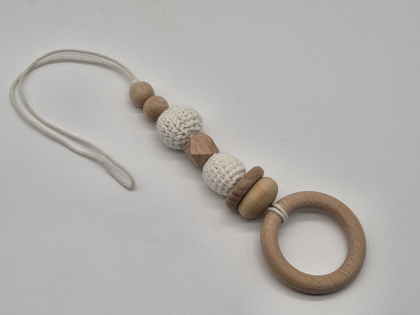 A wooden baby gym hanging toy with a crochet bead and a white cord, photographed on a light gray background.