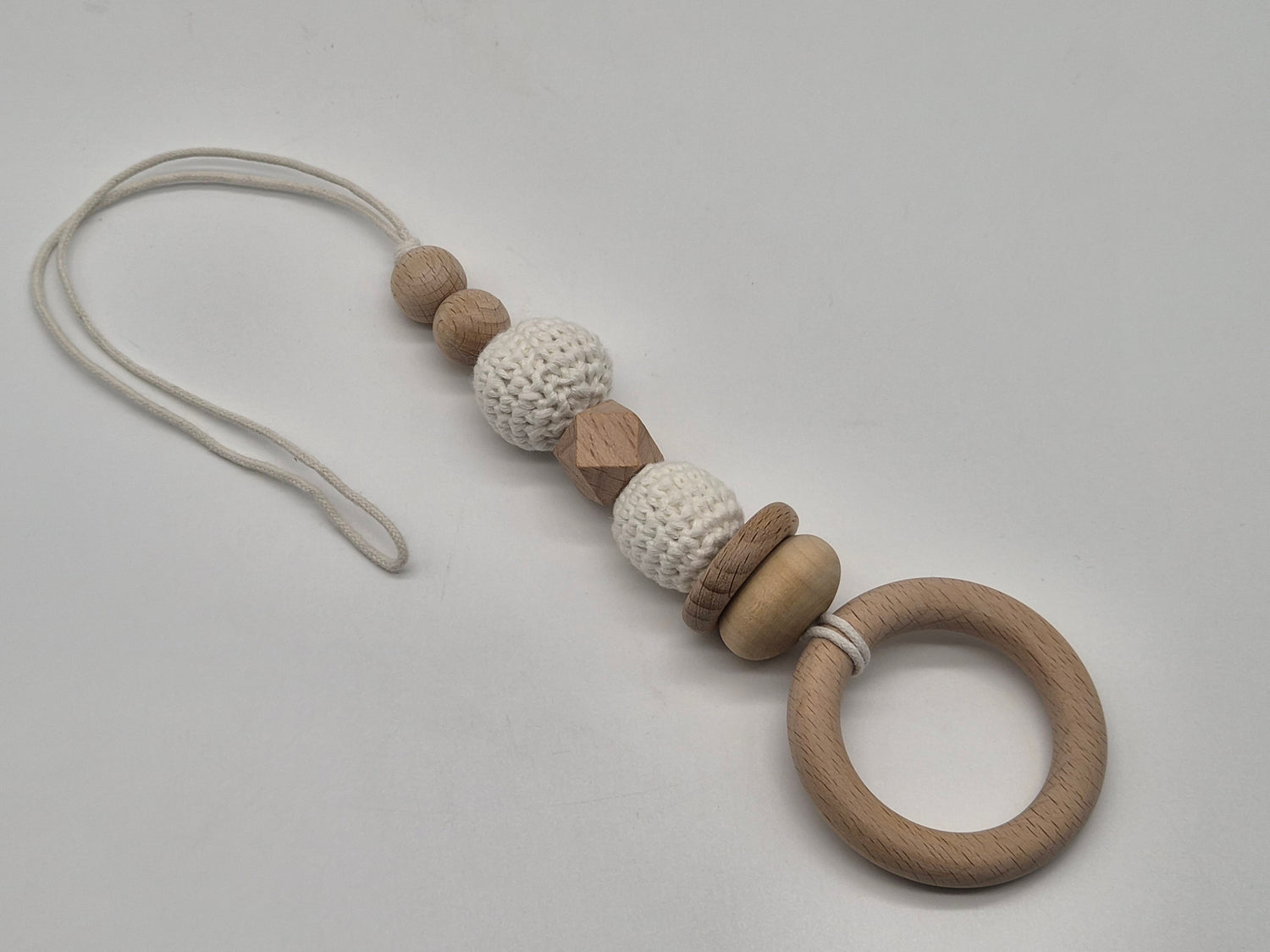 A wooden baby gym hanging toy with a crochet bead and a white cord, photographed on a light gray background.