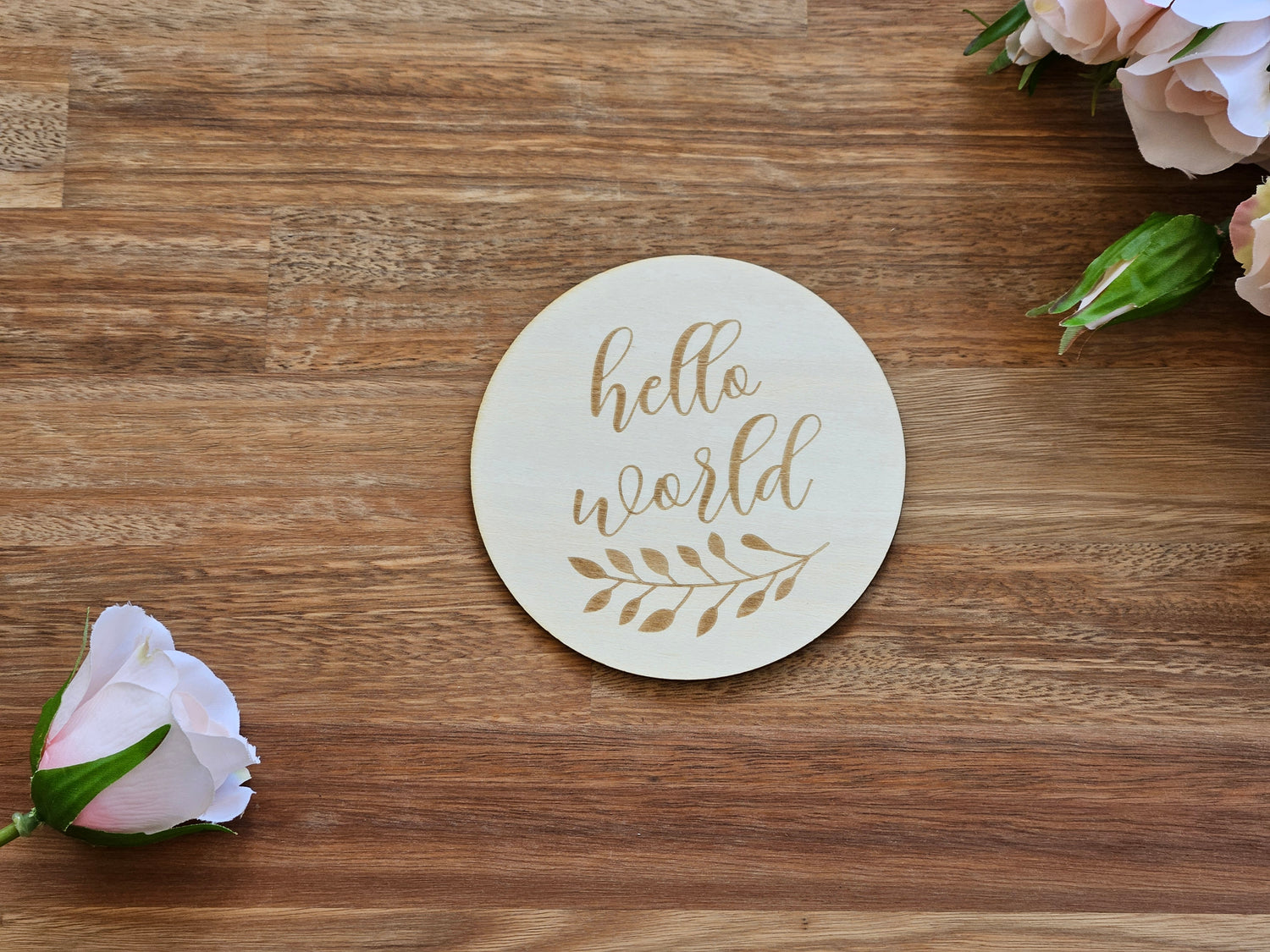 A round wooden disc with the words 'hello world' in gold cursive script and a gold leaf design, 
